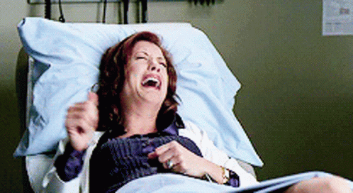 A Woman Is Laying In A Hospital Bed Laughing With Her Eyes Closed GIF