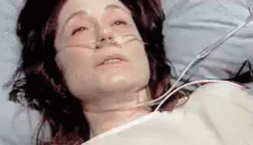 A Woman Is Laying In A Hospital Bed With An Oxygen Mask . GIF