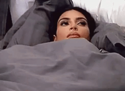 A Woman Is Laying In Bed Covered In A Blanket . GIF