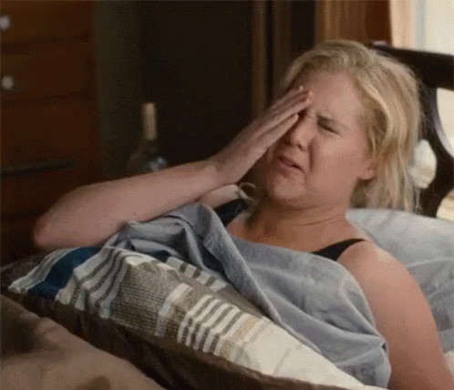 A Woman Is Laying In Bed Rubbing Her Eyes . GIF