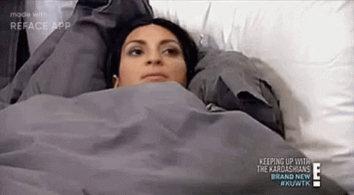 A Woman Is Laying In Bed Under A Blanket With Her Head On A Pillow . GIF