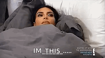 A Woman Is Laying In Bed Under A Blanket With The Words `` Im This '' Written On It . GIF