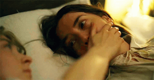 A Woman Is Laying In Bed With A Man Covering Her Mouth With Her Hand . GIF