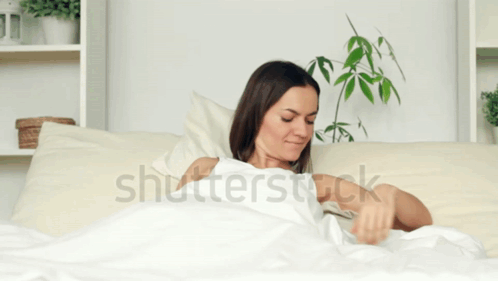 A Woman Is Laying In Bed With Her Arms Outstretched And The Word Shutterstock Is On The Bottom GIF