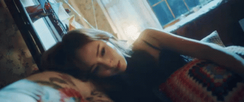 A Woman Is Laying In Bed With Her Head On A Pillow Looking At The Camera . GIF