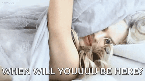 A Woman Is Laying In Bed With The Words `` When Will Youuu Be Here '' Written On The Bottom Of The Image . GIF