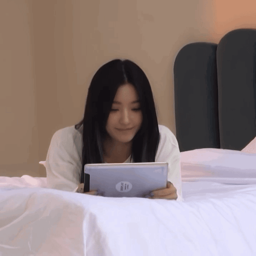 a woman is laying on a bed holding a hp tablet