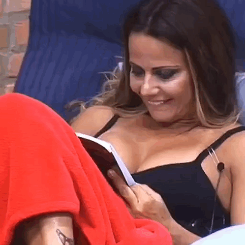 A Woman Is Laying On A Bed Reading A Book . GIF