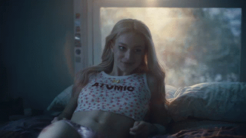 A Woman Is Laying On A Bed Wearing A Shirt That Says Atomic GIF