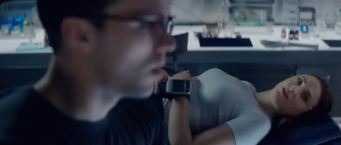 a woman is laying on a bed while a man looks at her watch