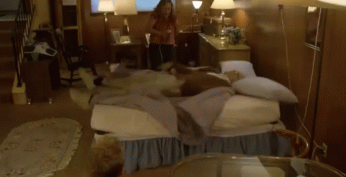 A Woman Is Laying On A Bed With A Bunch Of Pillows Flying Around Her . GIF