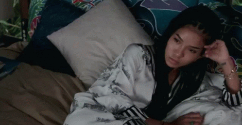 a woman is laying on a bed with a pillow and looking at the camera .