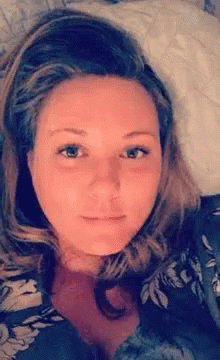 A Woman Is Laying On A Bed With A Pillow In Her Lap And Looking At The Camera . GIF