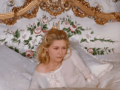 A Woman Is Laying On A Bed With Flowers On The Headboard GIF