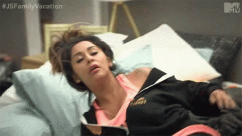 A Woman Is Laying On A Bed With Her Head On A Pillow And A Book . GIF