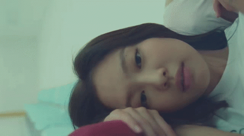 A Woman Is Laying On A Bed With Her Head On Her Hand GIF