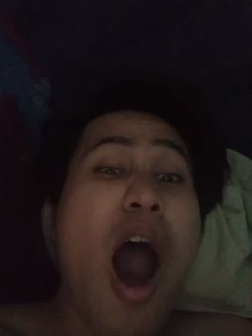 A Woman Is Laying On A Bed With Her Mouth Open And Her Tongue Sticking Out . GIF