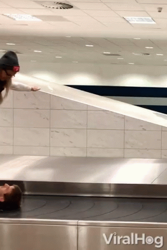 A Woman Is Laying On A Conveyor Belt Next To A Sign That Reads Viralhog GIF