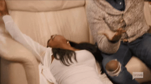 A Woman Is Laying On A Couch With Her Arms Outstretched While A Man Sits Behind Her .. GIF