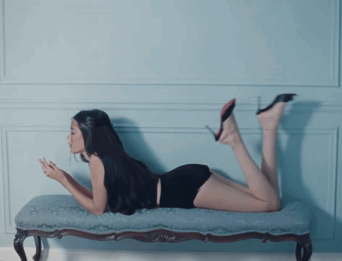 A Woman Is Laying On Her Stomach On A Bench And Looking At Her Phone GIF