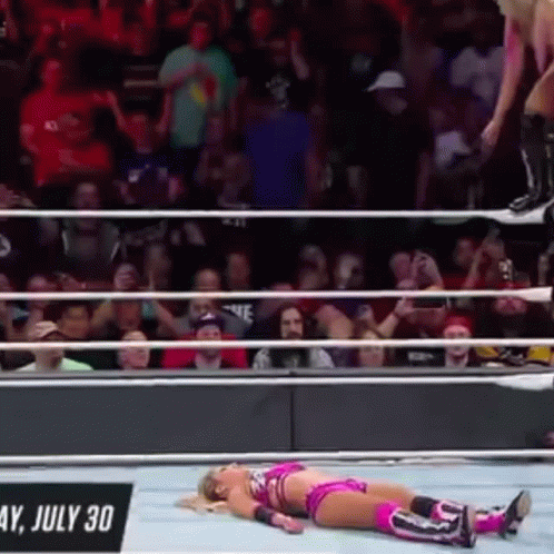 A Woman Is Laying On The Ground In A Wrestling Ring While A Man Jumps Over Her . GIF