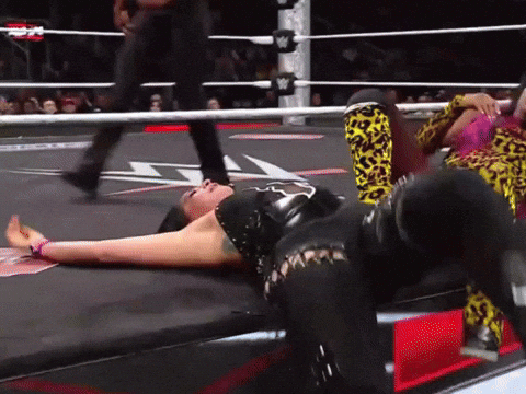 A Woman Is Laying On The Ground In A Wrestling Ring While A Referee Walks Behind Her GIF