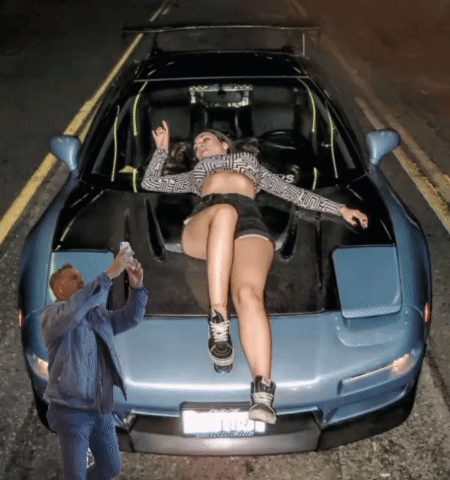 A Woman Is Laying On The Hood Of A Car While A Man Takes A Picture Of Her GIF