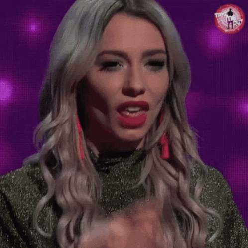 A Woman Is Licking Her Finger While Wearing Red Earrings And A Green Top GIF