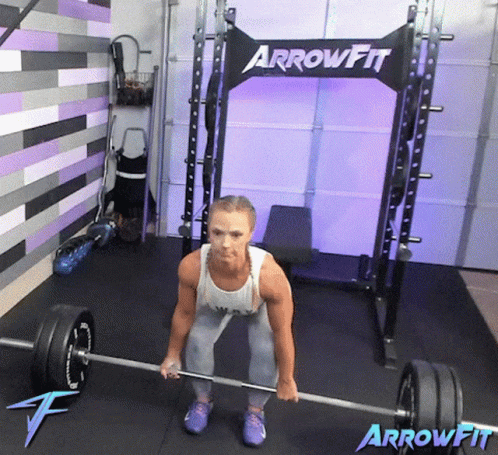 A Woman Is Lifting A Barbell In Front Of A Arrowfit Rack GIF