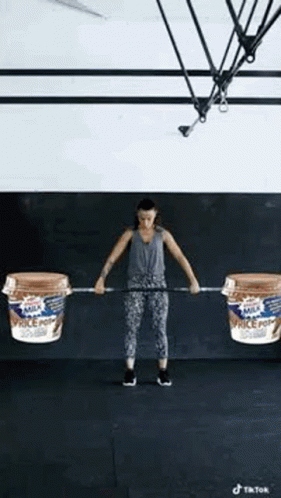 A Woman Is Lifting A Barbell With Two Containers Of Milk On It . GIF