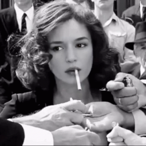 A Woman Is Lighting A Cigarette In A Crowd Of People GIF