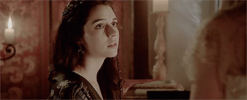 A Woman Is Looking At Another Woman In A Room With A Candle In The Background GIF