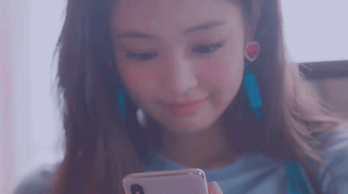 A Woman Is Looking At Her Phone And Smiling While Wearing Earrings . GIF