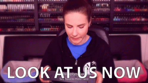 A Woman Is Looking At Her Phone With The Words Look At Us Now Behind Her GIF