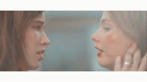 A Woman Is Looking At Her Reflection In A Mirror And Touching Her Face . GIF