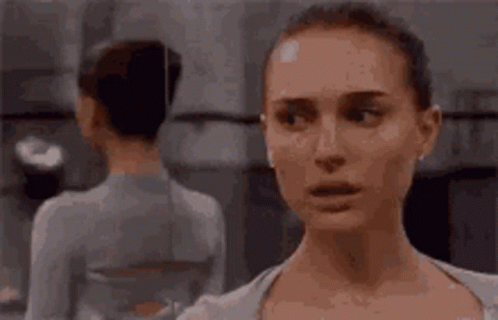A Woman Is Looking At Herself In The Mirror . GIF