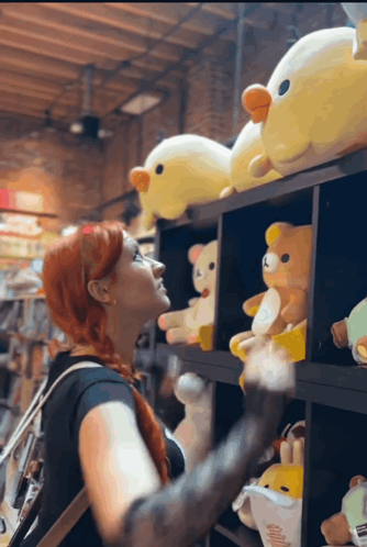 A Woman Is Looking At Stuffed Animals On A Shelf GIF