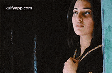 A Woman Is Looking Out Of A Window And Holding Her Hand To Her Chest . GIF