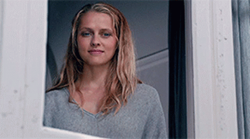 A Woman Is Looking Out Of A Window And Smiling . GIF