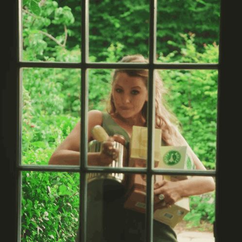 a woman is looking out of a window holding a box with a green circle on it