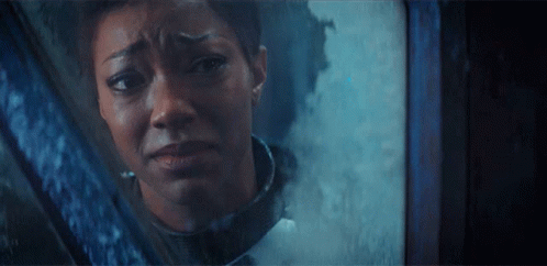 A Woman Is Looking Out Of A Window With A Sad Look On Her Face GIF