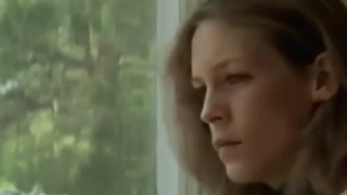 A Woman Is Looking Out Of A Window With A Serious Look On Her Face . GIF