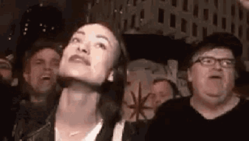 A Woman Is Looking Up At Something In A Crowd Of People At A Concert . GIF