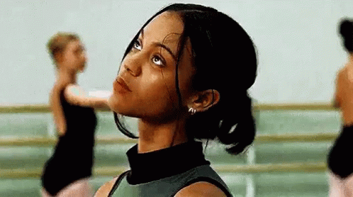A Woman Is Looking Up At The Sky In A Dance Studio While Other Dancers Are Dancing In The Background . GIF