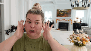 a woman is making a funny face in a living room while covering her ears with her hands .