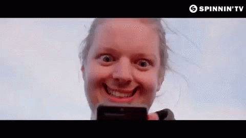 A Woman Is Making A Funny Face While Holding A Cell Phone In Her Hand . GIF