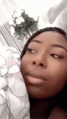 A Woman Is Making A Funny Face While Laying On A Bed With Flowers In The Background . GIF