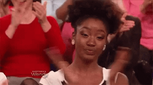 A Woman Is Making A Funny Face While Sitting In A Crowd Of People Clapping . GIF
