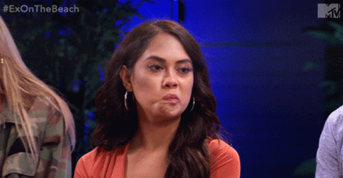 A Woman Is Making A Funny Face While Sitting In Front Of A Blue Wall With The Words Exon The Beach On It GIF