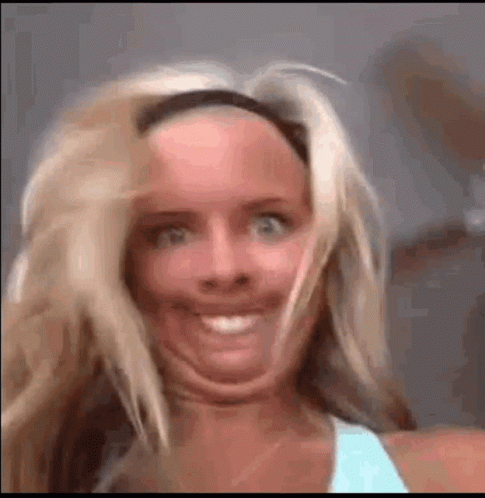 A Woman Is Making A Funny Face With Her Mouth Open And Her Hair Blowing In The Wind . GIF